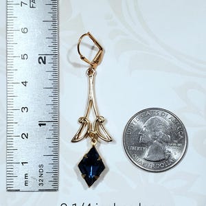 May include: Gold dangle earrings with a dark blue faceted gemstone. The earrings are 2 1/4 inches long.