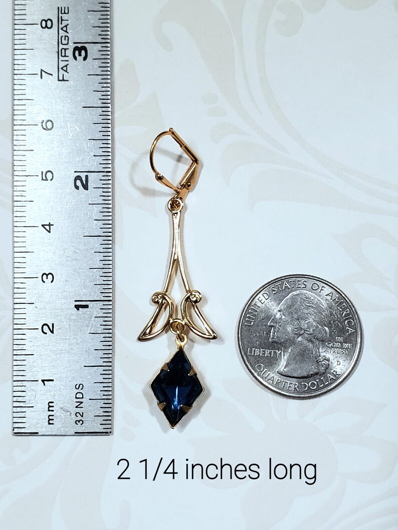 May include: Gold dangle earrings with a dark blue faceted gemstone. The earrings are 2 1/4 inches long.