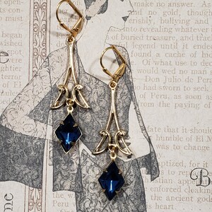 May include: A pair of gold dangle earrings with blue gemstone accents. The earrings feature a delicate, ornate design with a teardrop-shaped pendant.