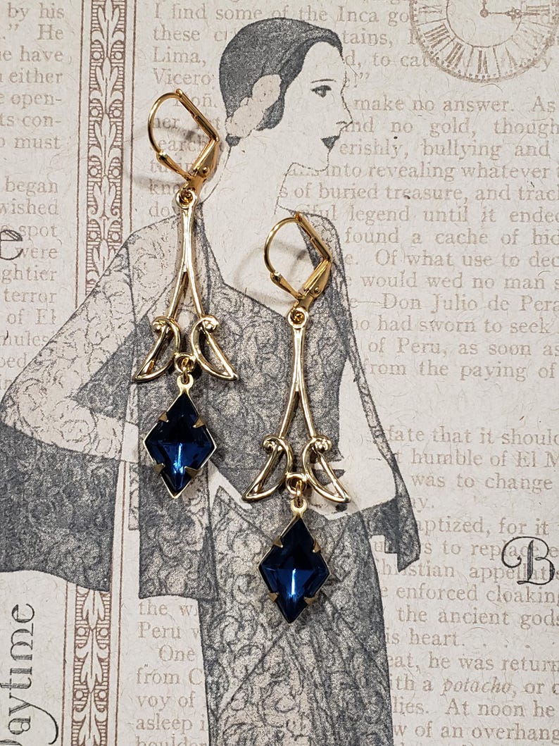 May include: A pair of gold dangle earrings with blue gemstone accents. The earrings feature a delicate, ornate design with a teardrop-shaped pendant.