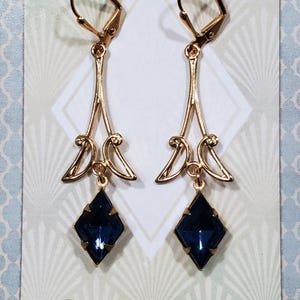 May include: A pair of gold dangle earrings with a dark blue gemstone pendant. The earrings feature a delicate, Art Deco-inspired design. The brand name "BOHEME BIJOU" is printed on the card.