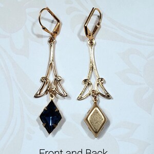May include: A pair of gold dangle earrings with a dark blue faceted gemstone on one side and a gold back on the other. The earrings have a delicate, ornate design.