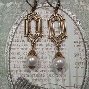 May include: A pair of gold-toned earrings with a geometric design and pearl accents. The earrings have a hook closure and are suspended from a delicate chain.