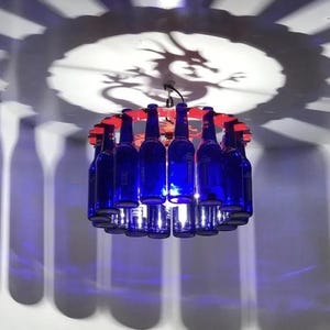 May include: A chandelier made from blue glass bottles with red accents. The bottles are arranged in a circle and hang from a metal frame.