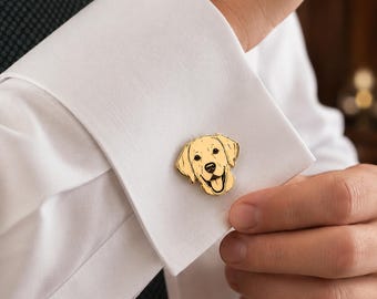 May include: A gold-coloured metal cufflink featuring a detailed, engraved illustration of a Golden Retriever dog head with a smiling expression, attached to the white fabric cuff of a long-sleeved dress shirt worn with a dark textured necktie.