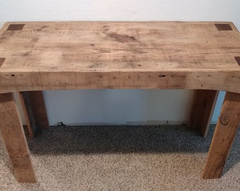 May include: A rustic wooden console table with a natural wood finish and a simple design. The table has a rectangular top and four legs. The top of the table has a distressed look with visible wood grain. The table is made of reclaimed wood and has a natural, earthy feel.