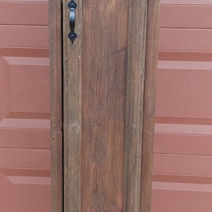 May include: A rustic wooden cabinet with a crescent moon cutout and black metal hinges and handle. The cabinet is painted a dark brown color and has a distressed finish.