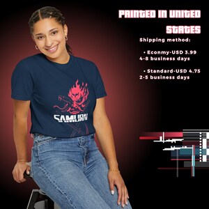 May include: Navy blue t-shirt featuring a pink graphic of a samurai mask with a snake and the word "SAMURAI". The text "PRINTED IN UNITED STATES" is at the top. The person is wearing blue jeans.