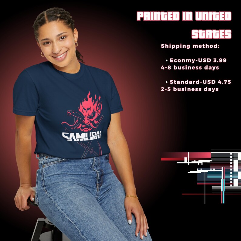 May include: Navy blue t-shirt featuring a pink graphic of a samurai mask with a snake and the word "SAMURAI". The text "PRINTED IN UNITED STATES" is at the top. The person is wearing blue jeans.