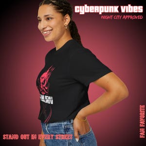 May include: Black t-shirt with a red graphic of a samurai mask and the text "SAMURAI" in white. The shirt also features the text "cyberpunk vibes" and "Night City Approved" in red. The phrase "Stand out in every street" is also visible.