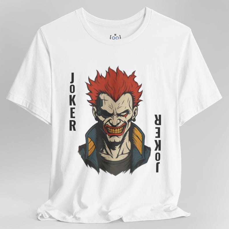 Peut inclure: T-shirt blanc avec un motif du Joker aux cheveux rouges et un sourire mena&ccedil;ant. Le mot "JOKER" est imprim&eacute; verticalement de chaque c&ocirc;t&eacute; de l'image. Le t-shirt a un col rond et des manches courtes.