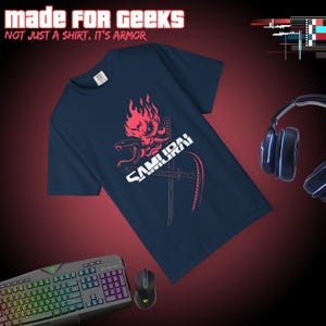 May include: Navy blue t-shirt with a red and white graphic of a samurai mask, swords, and the word "SAMURAI". The text "MADE FOR GEEKS" and "NOT JUST A SHIRT, IT'S ARMOR" are at the top. A gaming keyboard, mouse, and headphones are also visible.