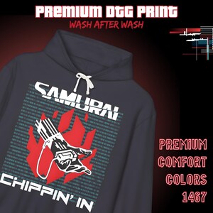 Op de afbeelding: Een donkergrijze hoodie met witte trekkoorden. De voorkant toont het woord "SAMURAI" boven een rood vlammenontwerp met een hand die een apparaat vasthoudt. Daaronder staat "CHIPPIN' IN". De tekst "PREMIUM DTG PRINT WASH AFTER WASH" staat bovenaan.