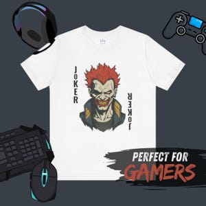 Peut inclure: T-shirt blanc avec un dessin du Joker aux cheveux roux et le mot "Joker" de chaque c&ocirc;t&eacute;. Le t-shirt a un col rond et des manches courtes. Le texte "PERFECT FOR GAMERS" est &eacute;galement visible.
