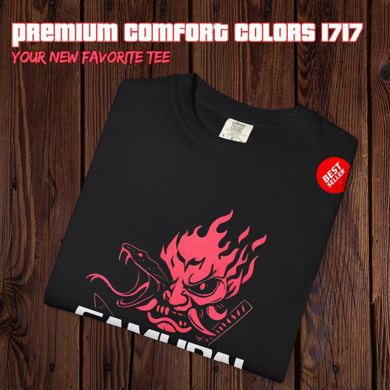 May include: Black t-shirt with a red graphic of a samurai mask and flames. The shirt has the text "SAMURAI" in white at the bottom. The top of the shirt has the text "PREMIUM COMFORT COLORS 1717" and "YOUR NEW FAVORITE TEE". A red "BEST SELLER" sticker is on the right.