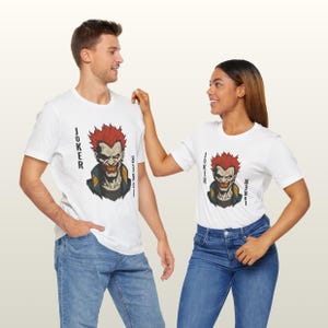 Peut inclure: T-shirts blancs avec un graphisme du Joker aux cheveux roux et un sourire sinistre. Le mot "JOKER" est imprim&eacute; verticalement sur les c&ocirc;t&eacute;s. Les mod&egrave;les portent des jeans bleus.