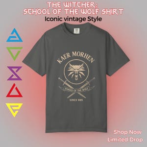 May include: Dark gray t-shirt with the text "THE WITCHER: SCHOOL OF THE WOLF SHIRT" and "Iconic vintage Style". The shirt features a circular design with a wolf head, crossed swords, and the words "KAER MORHEN" and "SCHOOL OF THE WOLF SINCE 995".