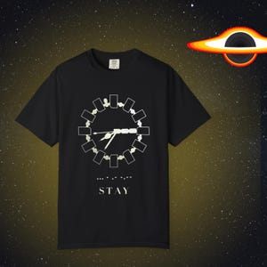May include: Black t-shirt with a white graphic of a clock-like design and the word "STAY" below. The design features a series of connected rectangles forming a circle with a central line and hands. The background is a starry night.