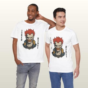 Peut inclure: Deux t-shirts blancs avec un graphisme d'un personnage roux avec le mot "JOKER" imprim&eacute; verticalement sur les c&ocirc;t&eacute;s. Le personnage a un sourire sinistre et porte une veste bleue avec des accents jaunes.