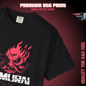 May include: Black t-shirt with a red graphic of a samurai mask with flames and swords. The word "SAMURAI" is printed in white at the bottom. The shirt has a crew neck and short sleeves. The text "PREMIUM DTG PRINT WASH AFTER WASH" is at the top.