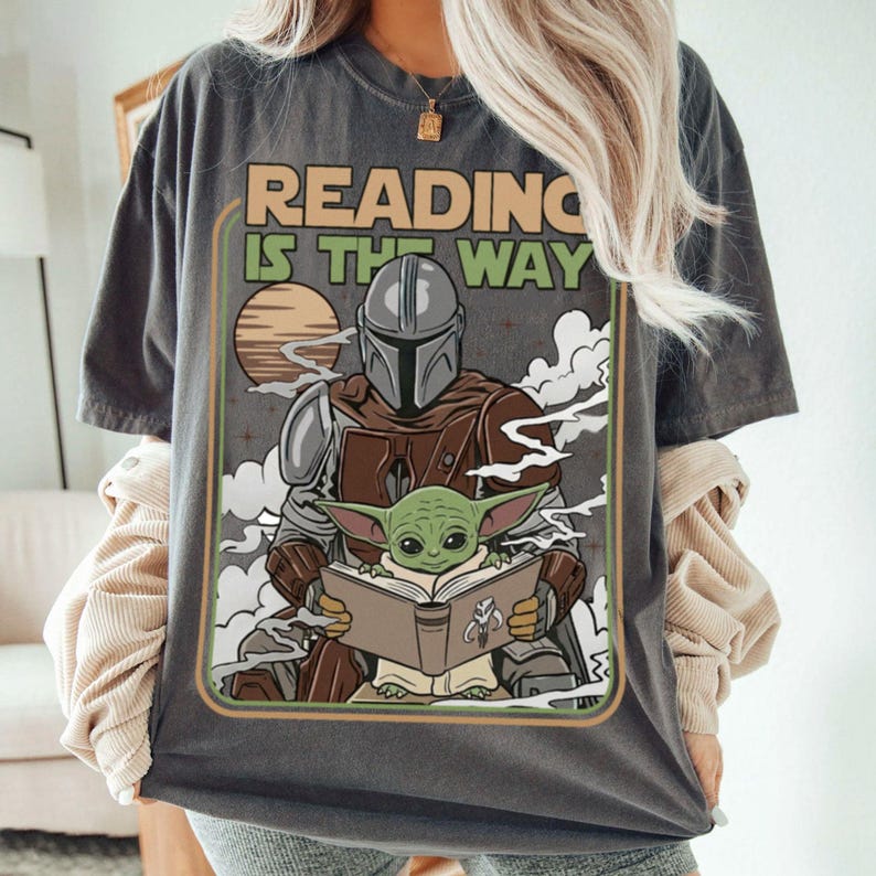 Puede incluir: Camiseta gris oscuro con un gr&aacute;fico retro de The Mandalorian y Grogu leyendo un libro, con el texto "READING IS THE WAY". El dise&ntilde;o incluye un atardecer y nubes.