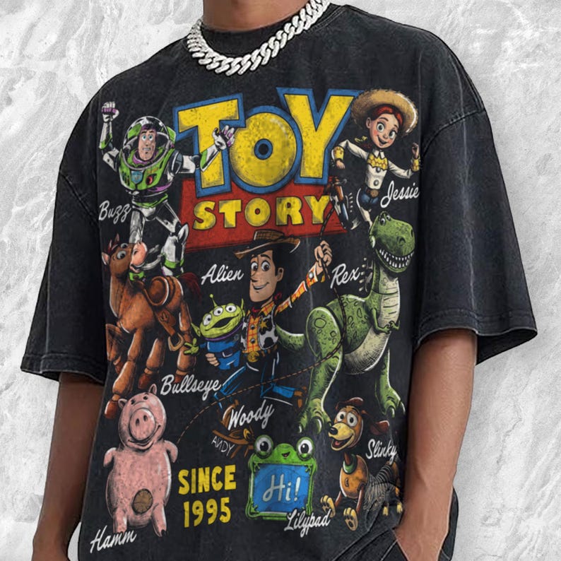Pode incluir: Uma t-shirt preta de manga curta com uma grande impress&atilde;o gr&aacute;fica de personagens de Toy Story, incluindo Buzz, Jessie, Woody, Rex, Bullseye, Hamm e um Alien. O texto diz Toy Story, Since 1995 e Hi! Lilypad. Acabamento de lavagem vintage.
