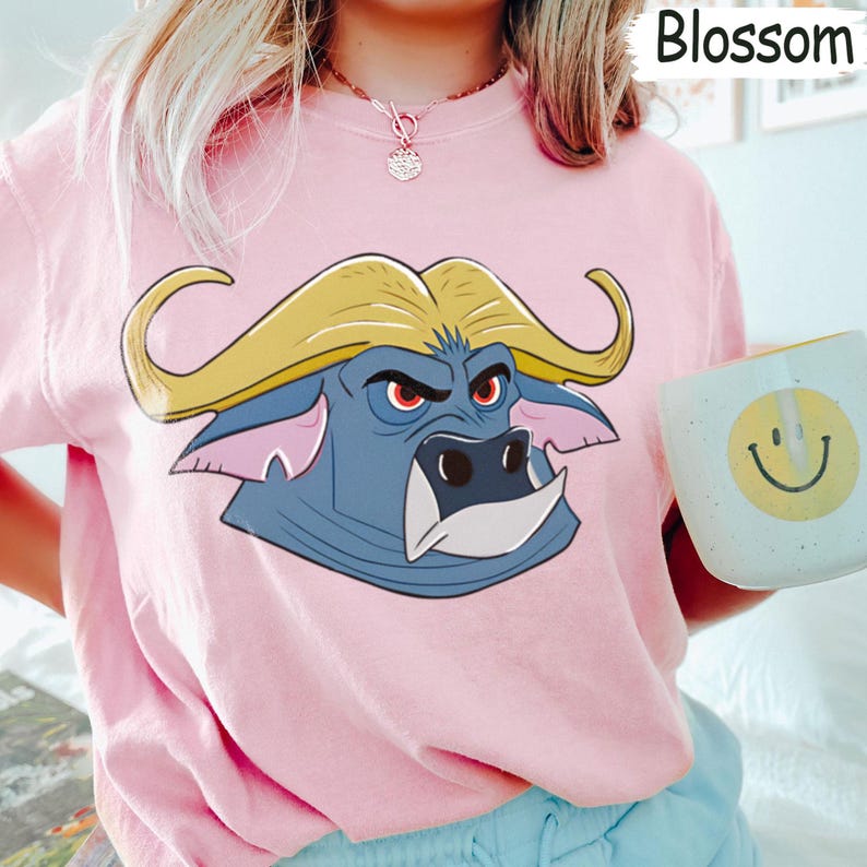 May include: Pink sweatshirt featuring a cartoon buffalo head with yellow hair and a stern expression. The buffalo is blue with pink ears and white tusks. The word "Blossom" is printed in white in the upper right corner.
