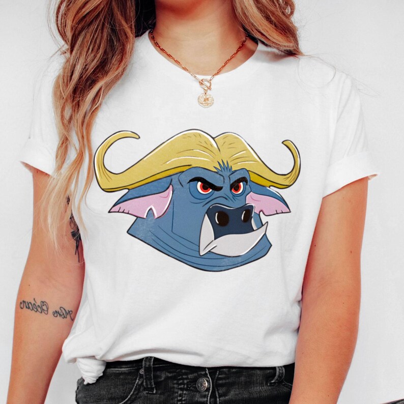 May include: White t-shirt featuring a cartoon buffalo head with yellow horns, blue face, and red eyes. The buffalo graphic is centered on the front of the shirt. The shirt has short sleeves and a crew neck.
