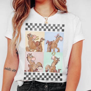 May include: White t-shirt featuring a cartoon horse design in four panels. The horse is brown with a saddle and a smiling expression. The design is framed by a black and white checkered pattern.