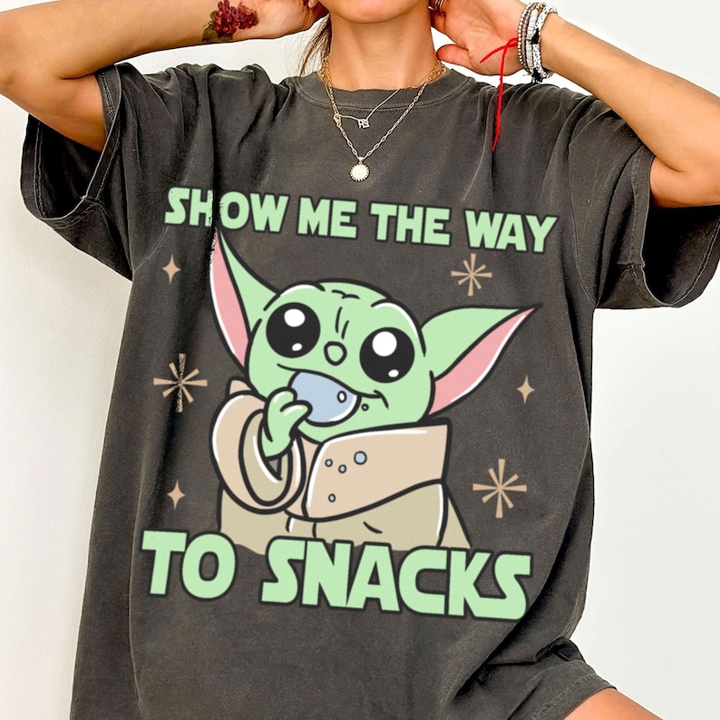 Peut inclure: T-shirt gris fonc&eacute; avec un personnage de dessin anim&eacute; vert tenant une collation. Le texte "SHOW ME THE WAY TO SNACKS" est imprim&eacute; au-dessus et en dessous du personnage en vert. Le t-shirt a une coupe d&eacute;contract&eacute;e.