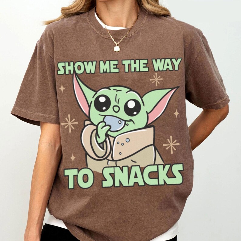 Peut inclure: T-shirt marron avec un personnage de dessin anim&eacute; vert aux grands yeux tenant une collation. Le texte "SHOW ME THE WAY TO SNACKS" est imprim&eacute; en vert au-dessus et en dessous du personnage. Le t-shirt a des manches courtes.
