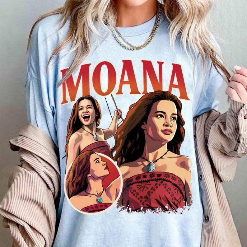 以下が含まれることがあります： 上部に大きな赤い文字でMOANAと書かれた水色のTシャツ。グラフィックには、赤い柄のチューブトップと青い石のペンダントが付いたネックレスを身に着けた、モアナというキャラクターのイラストが3つ描かれています。