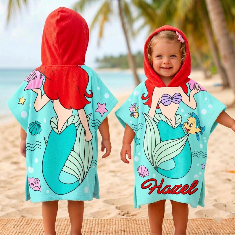 May include: Two children's hooded beach towels. The towels are light blue with a cartoon mermaid design, red hair, and a teal tail. The hood is red. One towel has the name "Hazel" in red script.
