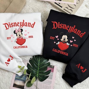Puede incluir: Sudaderas blancas y negras con bordado "Disneyland", Mickey y Minnie Mouse, y un coraz&oacute;n. Las sudaderas tambi&eacute;n presentan el texto "EST 1955 CALIFORNIA" e iniciales en las mangas.