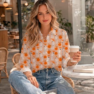 May include: A long-sleeve button-down shirt featuring a repeating pattern of white cockatoos and bright orange circles on a light beige background, paired with light blue denim jeans. The shirt has a classic collar and white buttons.