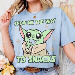 Peut inclure: T-shirt bleu clair avec un personnage de dessin anim&eacute; vert aux grands yeux tenant une collation. Le texte "SHOW ME THE WAY TO SNACKS" est imprim&eacute; en vert. Le t-shirt a des manches courtes.