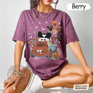 May include: Berry-colored t-shirt featuring a cartoon image of Mater from the movie Cars, decorated for Halloween. The design includes Mickey Mouse balloons, pumpkins, ghosts, and spiderwebs. The word "Berry" is printed at the top right.