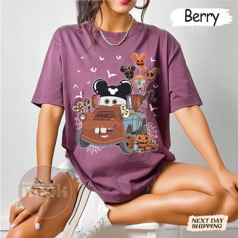 May include: Berry-colored t-shirt featuring a cartoon image of Mater from the movie Cars, decorated for Halloween. The design includes Mickey Mouse balloons, pumpkins, ghosts, and spiderwebs. The word "Berry" is printed at the top right.