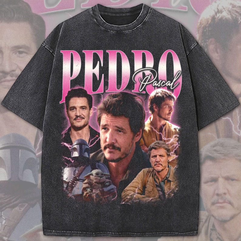 Op de afbeelding: Donkergrijs t-shirt met een vintage design. Het woord "PEDRO" staat in roze, met "Pascal" in script. De shirt heeft meerdere afbeeldingen van een man, met bliksemgraphics.