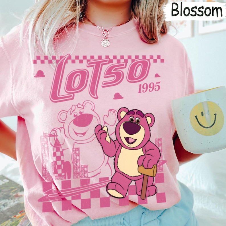 May include: Pink t-shirt featuring a graphic of Lotso the bear from Toy Story, with the text "Lotso 1995". The design includes a cartoon image of Lotso holding a mallet. The shirt is a light pink color.