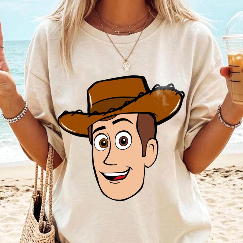 May include: Beige t-shirt featuring a cartoon illustration of a smiling cowboy character with a brown hat and a friendly expression. The design is centered on the shirt, offering a playful and recognizable image.