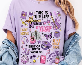 May include: A light purple t-shirt featuring a collage of graphics and text related to the Hannah Montana TV show. The design includes guitars, stars, butterflies, and phrases like "This is the Life" and "Best of Both Worlds".