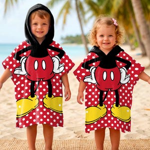 May include: Two children wearing red hooded ponchos with a white polka dot pattern. The ponchos feature a large Mickey Mouse design on the front, with black, white, red, and yellow colors. The children are standing on a sandy beach.