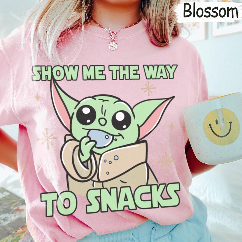 Peut inclure: T-shirt rose avec un dessin d'un personnage extraterrestre vert tenant une collation. Le texte "SHOW ME THE WAY TO SNACKS" est imprim&eacute;. Une tasse blanche avec un smiley jaune est visible.