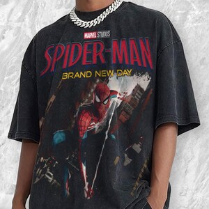 May include: Black t-shirt featuring a graphic of Spider-Man with the text "SPIDER-MAN BRAND NEW DAY" and the Marvel Studios logo. The superhero is depicted in a dynamic pose against a cityscape backdrop. The shirt has a vintage, worn look.