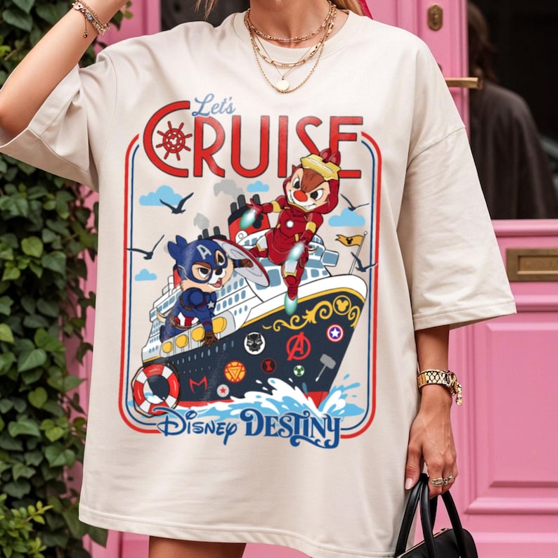 May include: Cream-colored t-shirt featuring a cartoon cruise ship with the text "Let's Cruise" and "Disney Destiny." The design includes cartoon characters in superhero costumes, a red and blue border, and nautical elements.