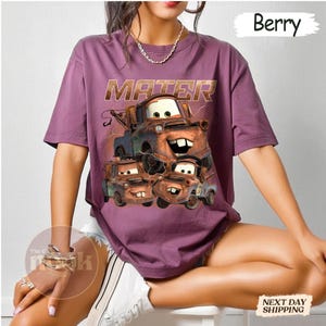 May include: Berry-coloured t-shirt featuring a graphic of the character Mater from the animated film Cars. The word "MATER" is printed above the character illustration. The shirt is a short-sleeved, casual style.