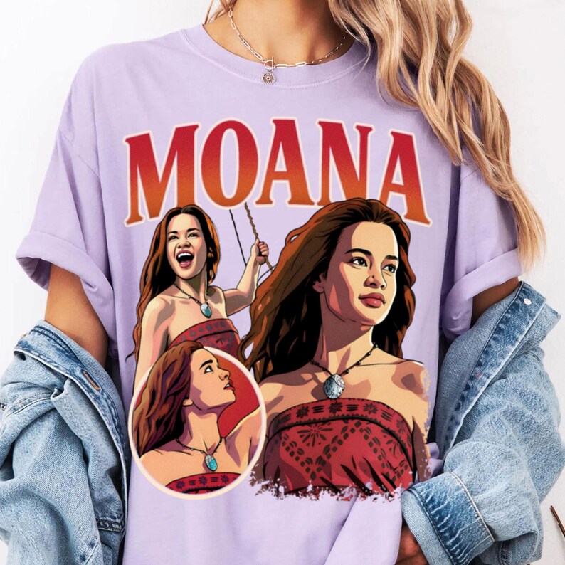 以下が含まれることがあります： 上部に大きな赤い文字でMOANAと書かれたライトパープルのTシャツ。グラフィックには、長い茶色の髪を持ち、赤い柄のトップスと青い石のネックレスを身に着けたキャラクター、モアナのイラストが3つ描かれています。