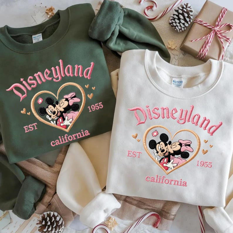 Peut inclure: Deux sweatshirts, un vert olive et un cr&egrave;me, brod&eacute;s avec "Disneyland" en rose. Chacun pr&eacute;sente un c&oelig;ur avec Mickey et Minnie Mouse, "EST 1955 California".