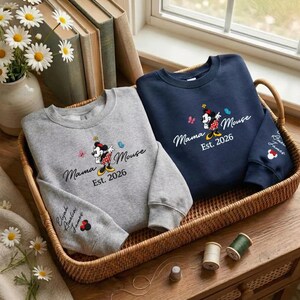 K&ouml;nnte beinhalten: Zwei Sweatshirts, eines grau und eines marineblau, mit einem Minnie-Mouse-Design. Das Design enth&auml;lt den Text "Mama Mouse Est. 2026" und eine Minnie-Mouse-Grafik. Das graue Sweatshirt hat die Namen "Elijah, Amelia, James" auf dem &Auml;rmel.